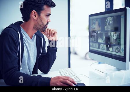 Keeping a close eye on things. a young man watching security footage on his computer. Stock Photo