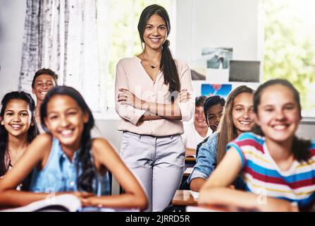 My students call me their favourite teacher. Portrait of an attractive young teacher standing with her arms folded in a classroom. Stock Photo
