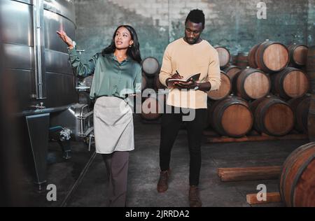 Man, woman and winemaker giving tour to new employee learning logistics in a winery or wood barrel distillery. Business owner or ceo working at Stock Photo