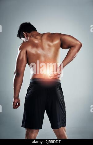 You can hurt your back if you go too heavy. Rearview shot of a sporty young man holding his back in pain against a grey background. Stock Photo