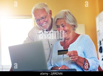 Time to spoil ourselves with a little help from technology. a senior couple using a laptop and credit card together at home. Stock Photo