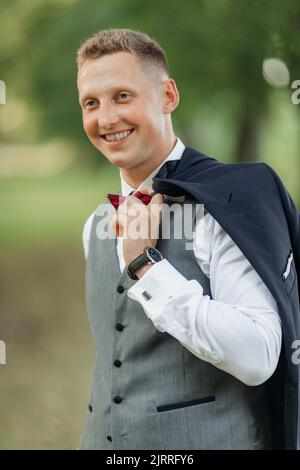 Vertical portrait of confident, cheerful, smiling blond businessman or groom in formal wear with watch holding jacket Stock Photo