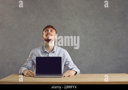 European cheerful man shows a laptop with a black screen on the table Stock Photo