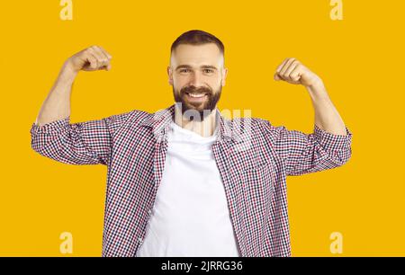 Cheerful man jokingly shows biceps demonstrating his strength on orange background. Stock Photo