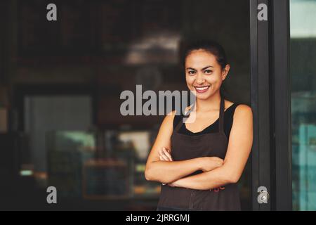 Ready to welcome you. Portrait of a young barista posing with her arms crossed in a coffee shot. Stock Photo
