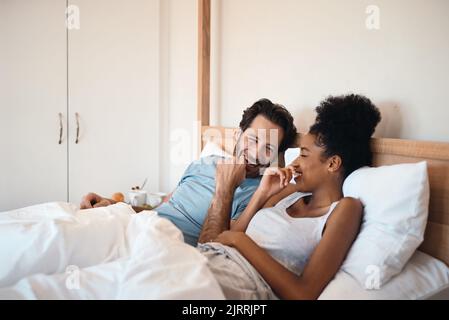 Happy, silly and goofy couple bonding in bed, sharing intimate relationship joke and moment. Young interracial husband and wife laughing, loving and Stock Photo