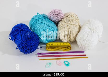 Cotton balls in blue, white, beige and pink colors next to a yellow measuring tape, pink, purple and gold metallic crochet hooks, pink and green stitc Stock Photo
