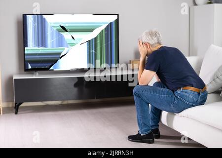 Frustrated Woman Sitting On Sofa Near Broken TV Screen Stock Photo