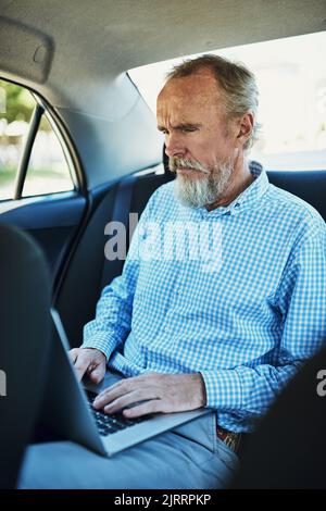 Places to go, people to see. a senior man using a laptop while traveling in the backseat of a car. Stock Photo