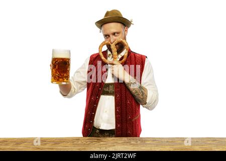 Portrait of young man wearing traditional Bavarian or German clothes smilling pretzel and holding beer glass isolated over white background Stock Photo