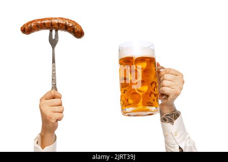 Male hands with grilled sausage on fork and mug with foamy lager beer isolated over white studio background. German and Bavarian holidays Stock Photo