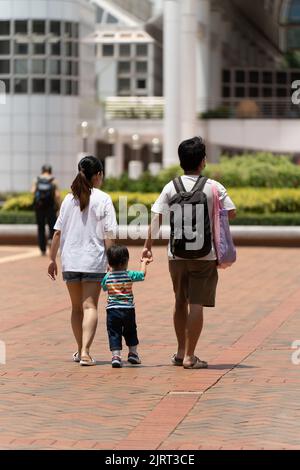 A vertical shot of the mummy and daddy holding hands of their child walking in the park Stock Photo