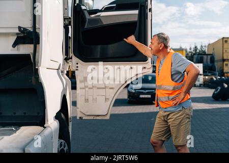 Portrait of caucasian mature man on semi-truck vehicles parking background. Truck driver worker  Stock Photo