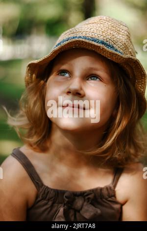 Cute blonde child 5 years old. Child in a straw hat. Portrait of a baby girl close-up. To look up. Stock Photo