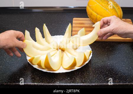 People take sliced ripe juicy melon slices from the plate with their hands. Delicious healthy food. Stock Photo