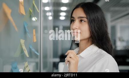 Arabian business lady managing daily tasks stand near board in office write reminder information instruction on paper sticky notes read stickers Stock Photo
