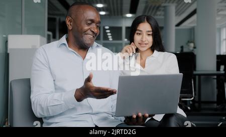 Diverse colleagues two business partners african arabian co-workers discuss internet project on laptop at office meeting planning working main tasks Stock Photo