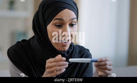Joyful islamic young woman in hijab smiling happily holding pregnancy test excited pregnant lady surprised and happy celebrating good news future Stock Photo