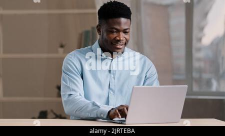 African american businessman professional worker male programmer man in blue shirt working freelance from home office typing email on laptop personal Stock Photo