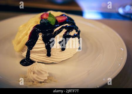 Delicious Pavlovai cake decorated with strawberries and blueberries with mint leaves and poured with white and dark chocolate. Stock Photo