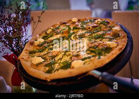 Delicious Italian pizza pizza with cheese, salmon and arugula leaves. Close-up photo with blurred background Stock Photo