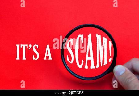 It's a scam text on red cover with hand holding magnifying glass. Scamming and fraud concept Stock Photo