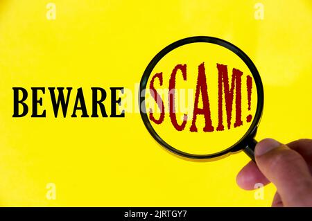 Beware scam text on yellow cover with hand holding magnifying glass. Scamming and fraud concept. Stock Photo