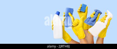 hand with yellow rubber glove holding cleaning supplies on blue background. banner with copy space Stock Photo