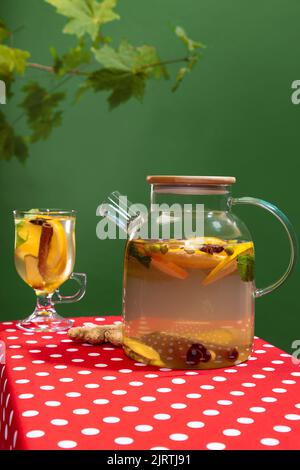 Teapot, kettle with delicious herbal tea with citrus, lemons, ginger and mint isolated over green background Stock Photo