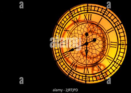 Glowing yellow-orange clock hanging on a dark wall. Stock Photo