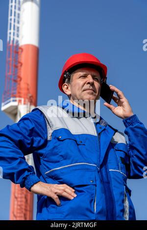 Man In Protective Workwear Using Mobile Phone In District Heating Power Plant. New Heating Season Uncertainty. Stock Photo