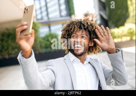 Joyful excited curly haired brazilian or african american stylish positive  woman, in green shirt, looks happily at the camera and smile, shows thumb  up gesture, stands on isolated yellow background Stock Photo 