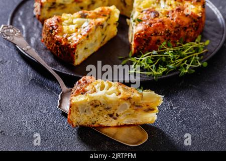 Cauliflower Cake with Pecorino Romano cheese, Basil and spices sliced on black platter on concrete table with a slice on cake shovel, horizontal view Stock Photo