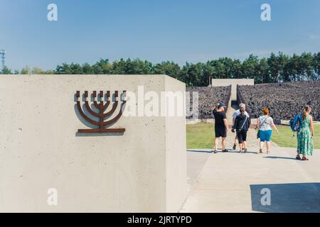 08.27.2022 - Belzec, Poland - Belzec Nazi Death Camp. Short conrete wall with metal menora symbol in front of entrance to former nazi death camp. Tourists at Holocaust memorial. Horizontal shot. High quality photo Stock Photo