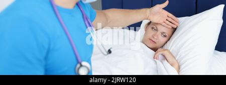 Doctor keeps hand on forehead of sick woman on bed Stock Photo