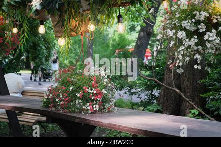 beautiful romantic place at street cafe in a park. wooden table decorated with flowers and wicker baskets. lamps hanging over a table. place for getting rest and dating Stock Photo