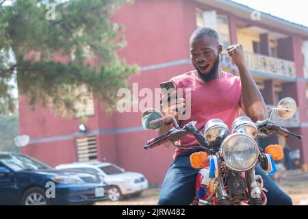 african bike man rejoices while checking his phone Stock Photo