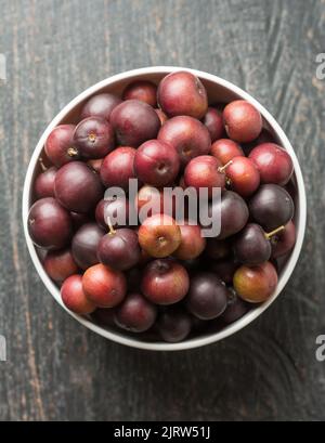 bowl full of governor's plum fruits, flacourtia indica, also known as ramontchi, madagascar plum or indian plum,reddish black fleshy fruits Stock Photo