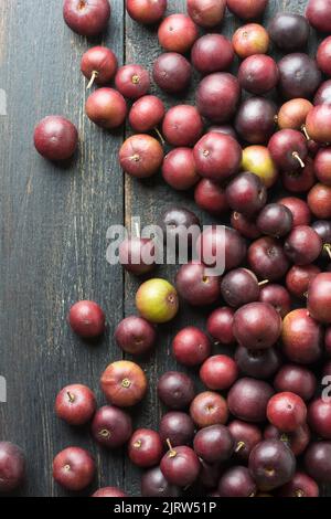 scattered governor's plum fruits on a black rustic table top, flacourtia indica, also known as ramontchi, madagascar plum or indian plum Stock Photo