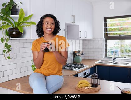A young multi-ethnic woman sits on her kitchen countertop enjoying breakfast Stock Photo