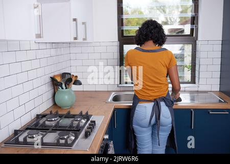 A young woman does dishes at the kitchen sink in small apartment Stock Photo