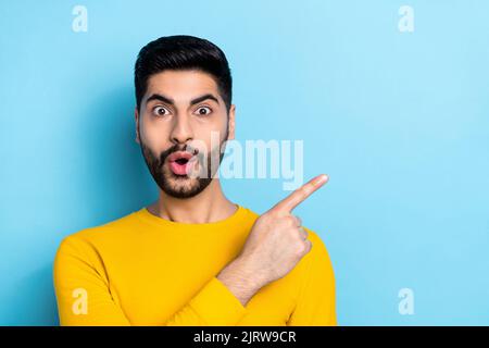 Photo of funny impressed guy dressed yellow pullover pointing finger empty space isolated blue color background Stock Photo
