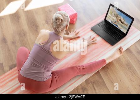 woman with laptop having online yoga class Stock Photo
