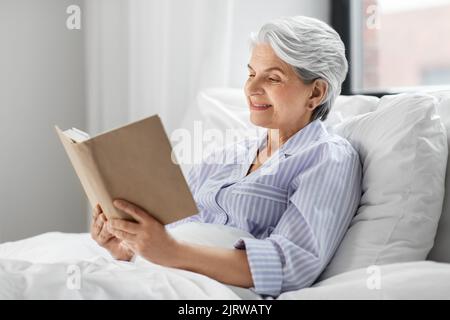 senior woman reading book in bed at home bedroom Stock Photo