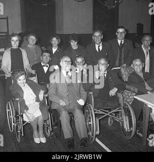 1965, historical, Red Cross tea party for disabled people, group picture showing volunteers standing with their guests in their wheelchairs, Fife, Scotland, UK. A leading charity, the British Red Cross, provides support to older, vulnerable people, helping them live independently in their own homes. The charity also supports the NHS; helping patients get home from hospital, easing patient flow and dealling with their immediate needs. The principles of the Red Cross are; humanity, impartiality, neutrality, independence, voluntary service, unity and universality. Stock Photo