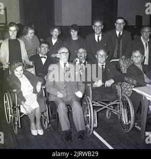 1965, historical, Red Cross tea party for disabled people, group picture showing volunteers standing with their guests in their wheelchairs, Fife, Scotland, UK. A leading charity, the British Red Cross, provides support to older, vulnerable people, helping them live independently in their own homes. The charity also supports the NHS; helping patients get home from hospital, easing patient flow and dealling with their immediate needs. The principles of the Red Cross are; humanity, impartiality, neutrality, independence, voluntary service, unity and universality. Stock Photo