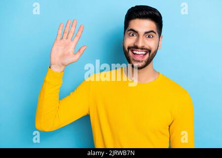 Photo of excited funny young guy dressed yellow pullover smiling waving arm palm isolated blue color background Stock Photo