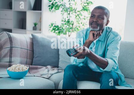 Photo of dreamy handsome mature man spend free time watching tv show sitting comfy sofa relaxing at home Stock Photo
