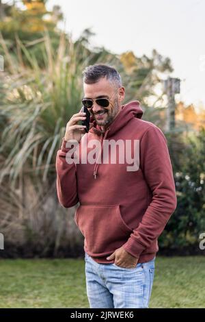 Handsome man talking on his smartphone in the backyard of his home Stock Photo