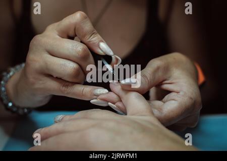 The hands of the manicurist paint the nails on the client's hand with varnish Stock Photo